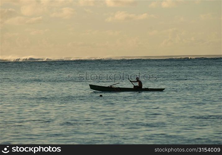 Silhouette of a man rowing a boat in the sea, Moorea, Tahiti, French Polynesia, South Pacific