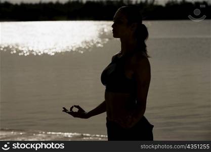 Silhouette of a mid adult woman meditating on the beach