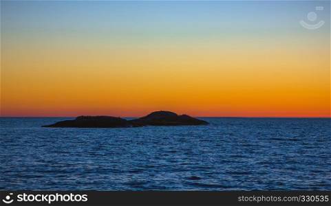 Silhouette of a small island on a background of orange sky horizon separated from the blue surface of the water.. White Night on Lake Onega