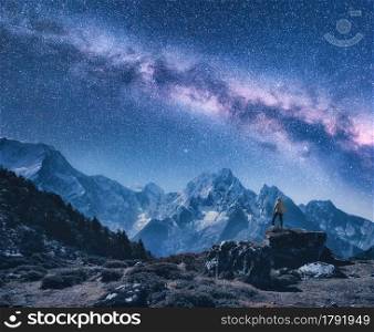Silhouette of a standing man on the stone, mountains and starry sky with Milky Way at night in Nepal. Sky with stars. Travel. Night landscape with snow-covered rocks and purple milky way. Space