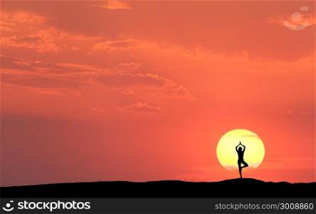 Silhouette of a standing sporty woman practicing yoga with raised up arms on the hill on the background of sun and colorful orange sky with clouds. Landscape with meditating girl at sunset. Fitness