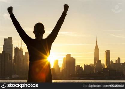 Silhouette of a successful woman or girl arms raised celebrating at sunrise or sunset in front of the New York City Skyline