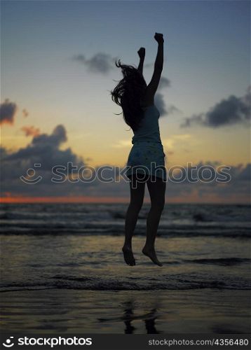 Silhouette of a teenage girl jumping on the beach at dusk