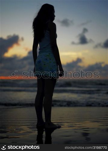 Silhouette of a teenage girl standing on the beach at dusk