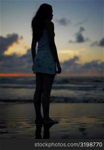 Silhouette of a teenage girl standing on the beach at dusk
