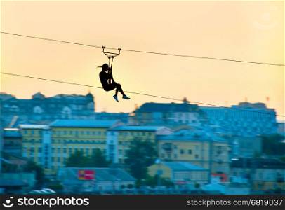 Silhouette of a woman on a zipline above the city. Motion blur