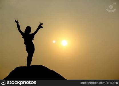 Silhouette of a woman practicing yoga on a rock.