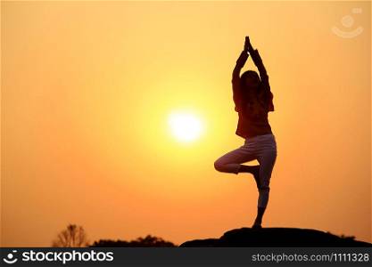 Silhouette of a woman practicing yoga on a rock.