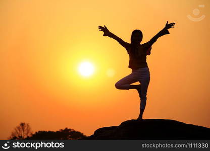 Silhouette of a woman practicing yoga on a rock.