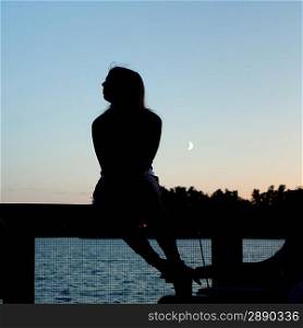 Silhouette of a woman sitting on a railing, Lake of the Woods, Ontario, Canada