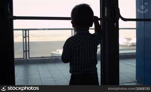 Silhouette of a young boy looking through a window in the airport to the airplanes in the landing strip