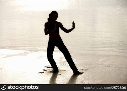 Silhouette of a young woman practicing martial arts on the beach