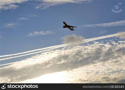 Silhouette of airplane in air with trails, low angle view