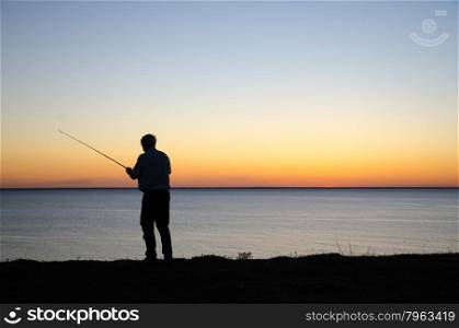 Silhouette of an angling man by a colorful sunset