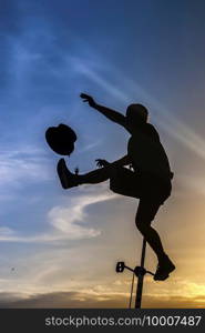 Silhouette of an equilibrist riding an unicycle, making some juggling with a top-hat. Equilibrist on a unicicle performing at sunset