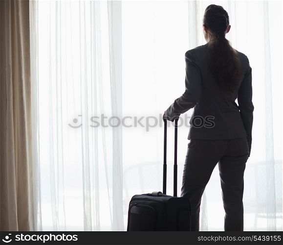 Silhouette of business woman with wheel bag looking into hotel window . rear view