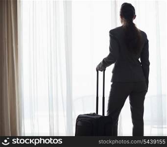 Silhouette of business woman with wheel bag looking into hotel window . rear view