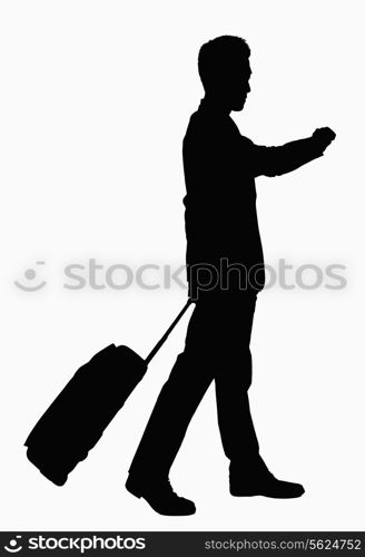 Silhouette of businessman checking wristwatch and pulling suitcase.