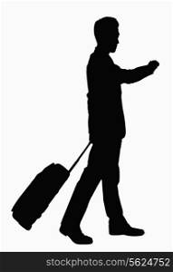 Silhouette of businessman checking wristwatch and pulling suitcase.