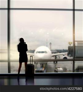 silhouette of businesswoman which expects flight aboard the plane in airport