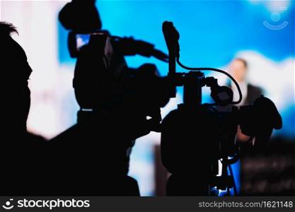 Silhouette of cameraman at media press conference recording presentation of a blurred speake, live streaming concept