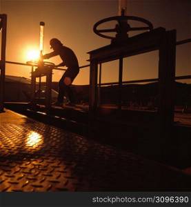 Silhouette of chemical plant worker turning valve