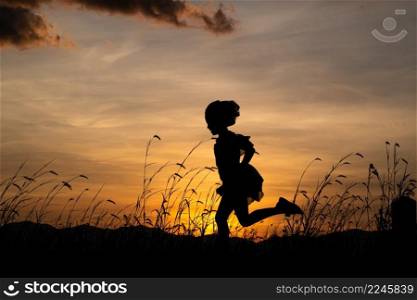 Silhouette of child girl running on the meadow at sunset background.