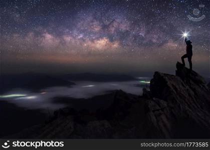 Silhouette of climber or backpacker. In his hand, he held the light up high above his head. Standing on rocky mountain peak and Milky Way Galaxy, success, winner, leader concept. High iso with Noise.. Leader and Milky Way Galaxy landscape.