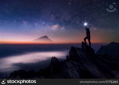 Silhouette of climber or backpacker. In his hand, he held the light up high above his head. Standing on rocky mountain peak and Milky Way Galaxy, success, winner, leader concept. High iso with Noise.. Leader on top.
