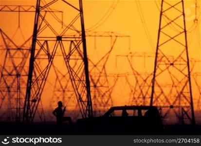 Silhouette of construction worker, car and electricity pylons with sunset in background