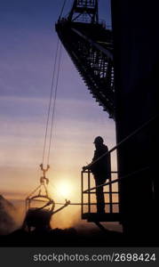 Silhouette of construction worker on construction site watching crane and digging bucket