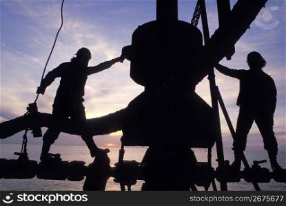 Silhouette of construction workers standing on precarious rigging with ocean in background