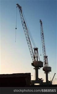 Silhouette of Cranes at Work in Boatyard and Blue Sky in background