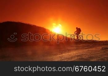 Silhouette of cyclist riding bicycle into the rising sun