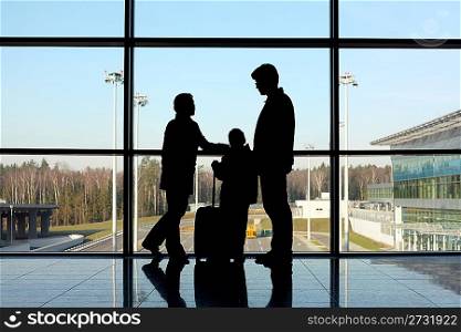 silhouette of family with luggage standing near window in airport