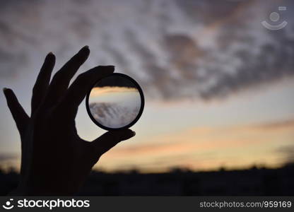 silhouette of female hand holding the lense and the blue sky on the background at the time of the sunset