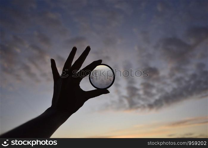 silhouette of female hand holding the lense and the blue sky on the background at the time of the sunset