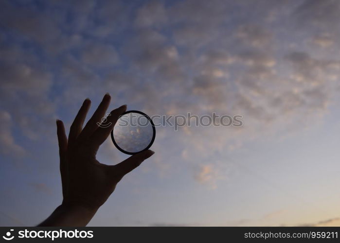 silhouette of female hand holding the lense and the blue sky on the background at the time of the sunset