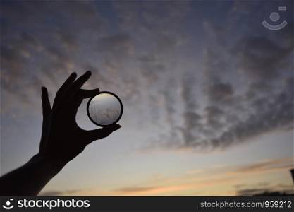 silhouette of female hand holding the lense and the blue sky on the background at the time of the sunset