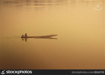 Silhouette of fisherman in boat on the river. Warm light tone concept.