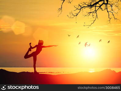 Silhouette of fitness athlete practicing yoga pose meditating at beach sunset. Woman stretching doing morning meditation against beautiful sky background.Zen wellness and wellbeing concept.