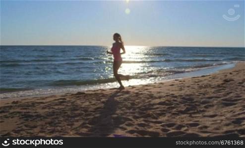 Silhouette of fitness athletic girl jogging along the beach long shot