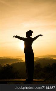 silhouette of free cheering woman open arms at mountain peak sunrise
