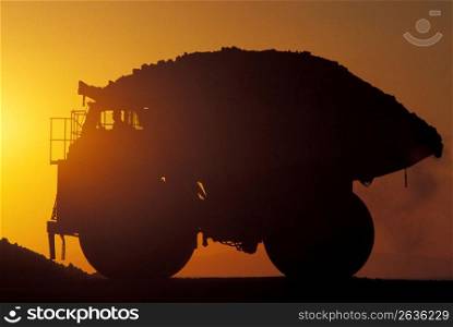 Silhouette of full dump truck with sunset in background