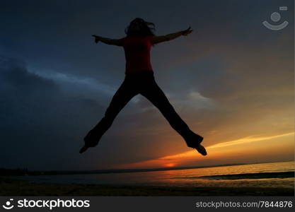 silhouette of full length of fitness sporty woman jumping on the beach at the sunset or sunrise
