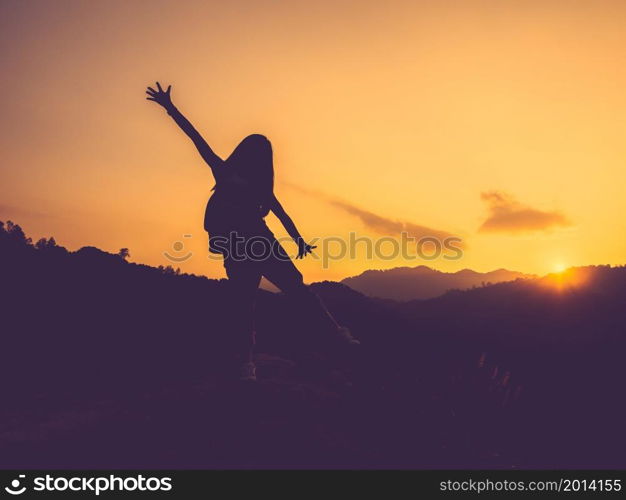 Silhouette of happy woman with open arms on peak of mountain at sunset.