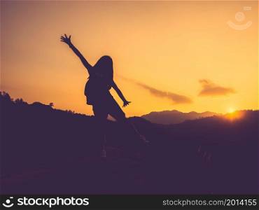 Silhouette of happy woman with open arms on peak of mountain at sunset.