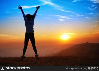 Silhouette of happy young woman jumping against sunset in the mountains