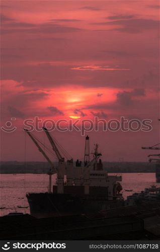 Silhouette of heavy crane tool in ship port and contain stock at sunset scene