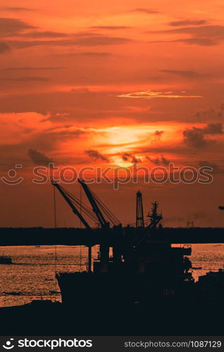 Silhouette of heavy crane tool in ship port and contain stock at sunset scene